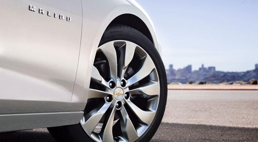 View of new tires on a Chevy Malibu with a cityscape in the background on a sunny day