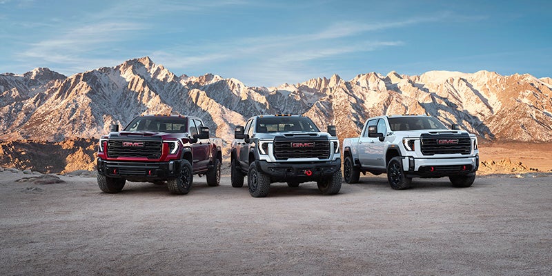 Thee 2024 GMC Sierra 2500s parked next to one another with mountains in the background