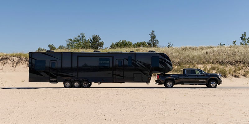 A black 2024 GMC Sierra 3500 parked with an extra large black trailer hitched to the back in an arid landscape