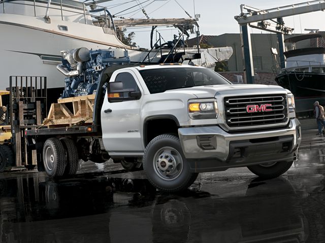 A white 2024 GMC Sierra 3500 Chassis Cab hauling an excavator in the rain